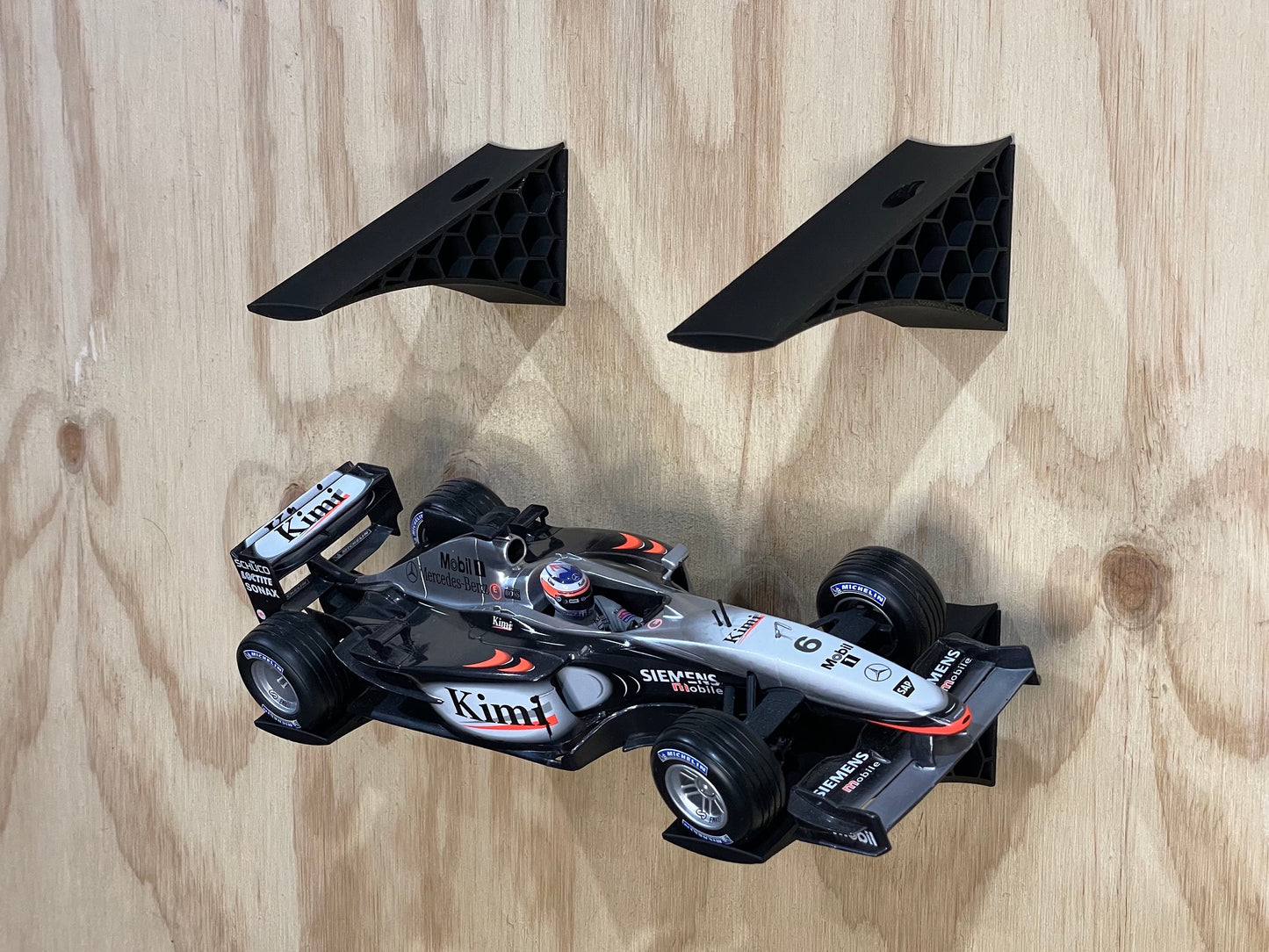 A set of two black angled display mounting brackets designed for 1:18 scale model cars, pictured with a toy race car mounted on them.