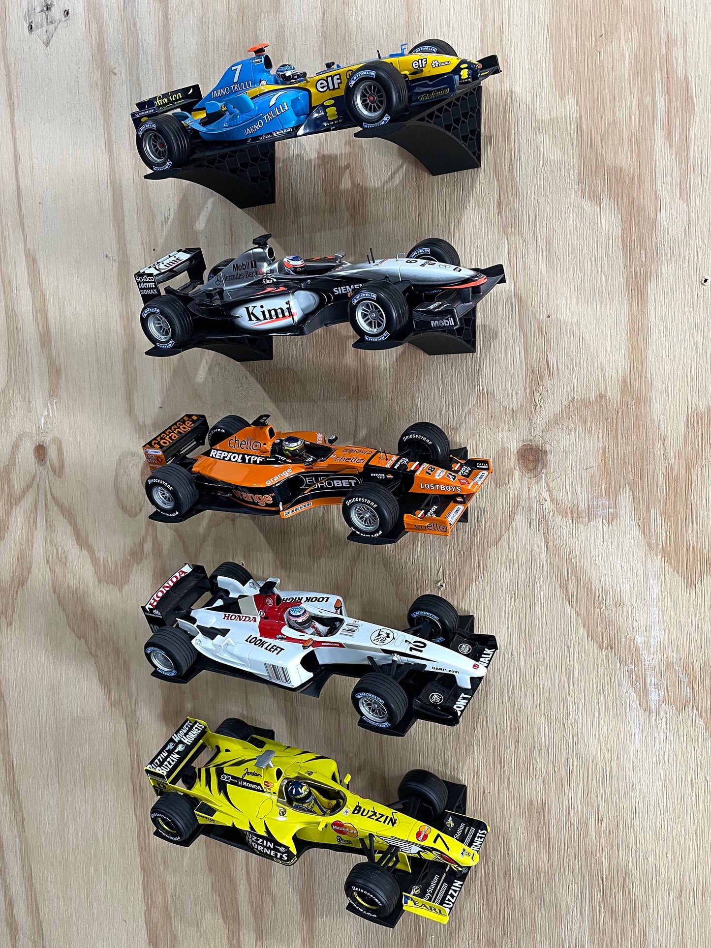 1:18 scale model car wall display using angled wall-mounted brackets for Formula 1 diecast cars, shown installed on plywood with five classic F1 models.