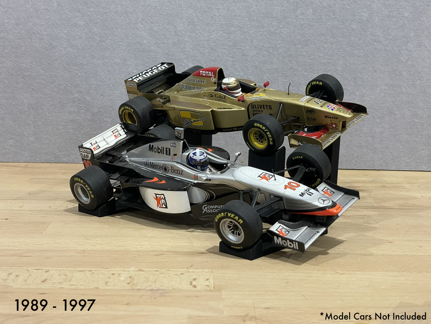Two 1:18 model Formula 1 cars on stands against a gray background