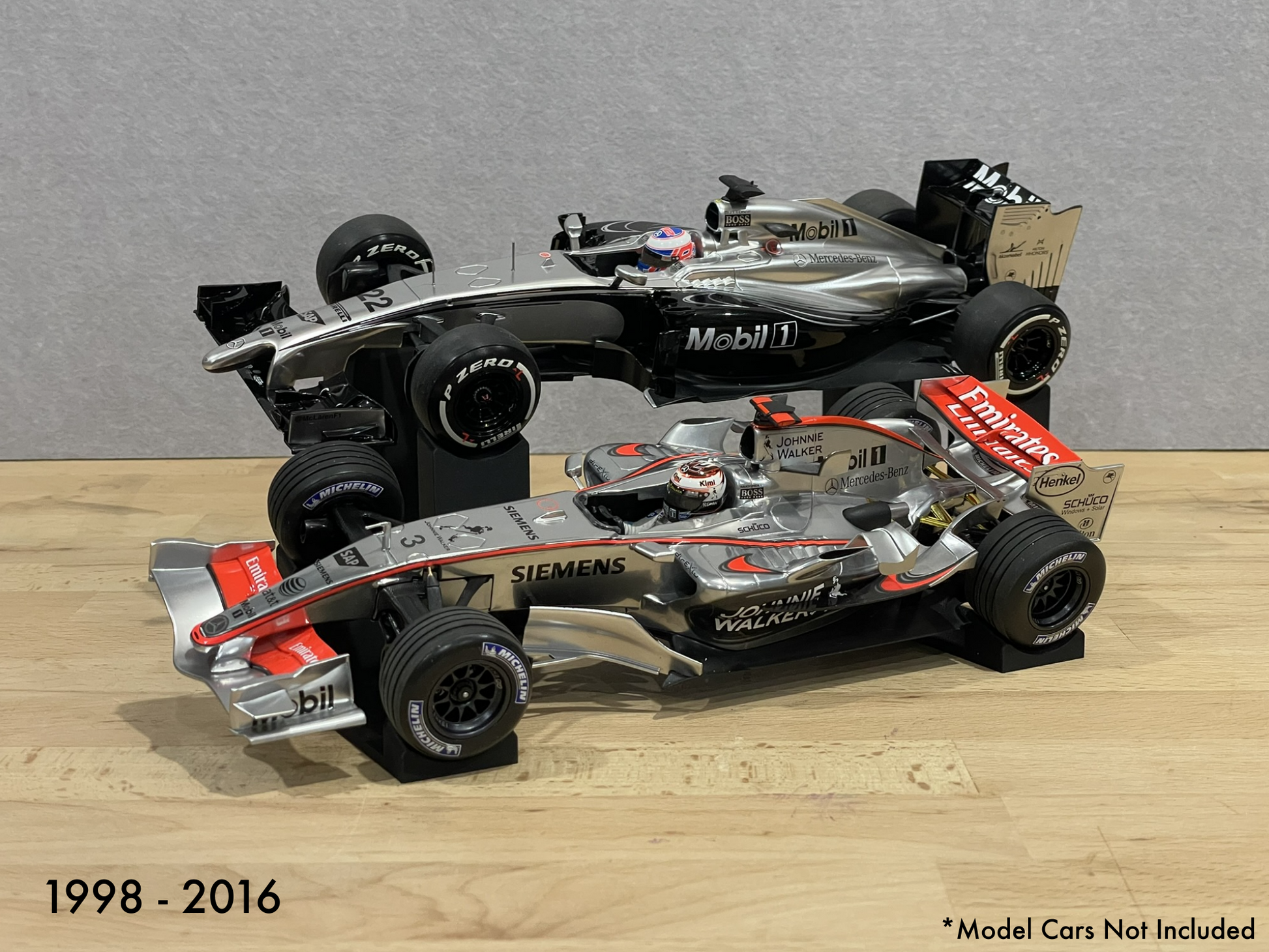 Two 1:18 model Formula 1 cars on stands against a gray background