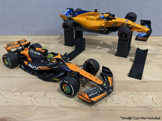 Two 1:18 model McLaren Formula 1 cars on stands against a gray background