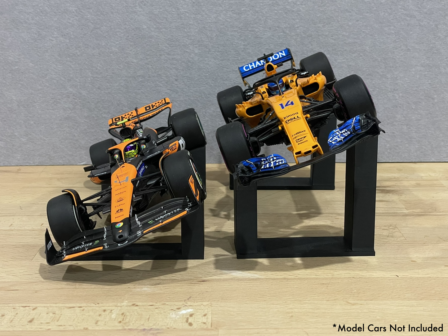 Two 1:18 model McLaren Formula 1 cars on stands against a gray background