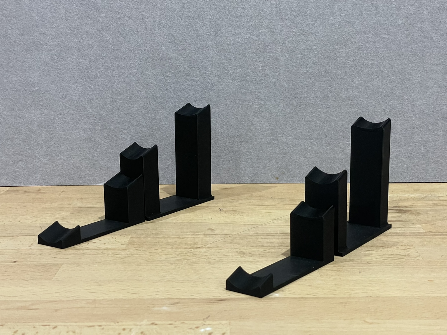 Set of black 3D printed angled display mounts for 1:18 scale model formula 1 cars, shown on a wooden surface, designed to cradle the front and rear axles securely.