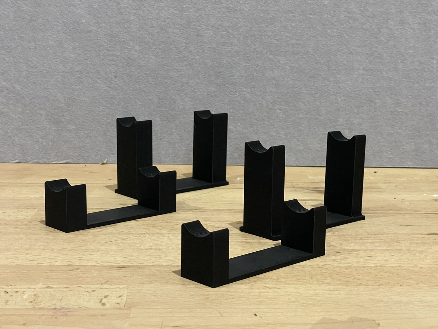 Set of black 3D printed level display riser mounts for 1:18 scale model formula 1 cars, shown on a wooden surface, designed to cradle the front and rear axles securely.