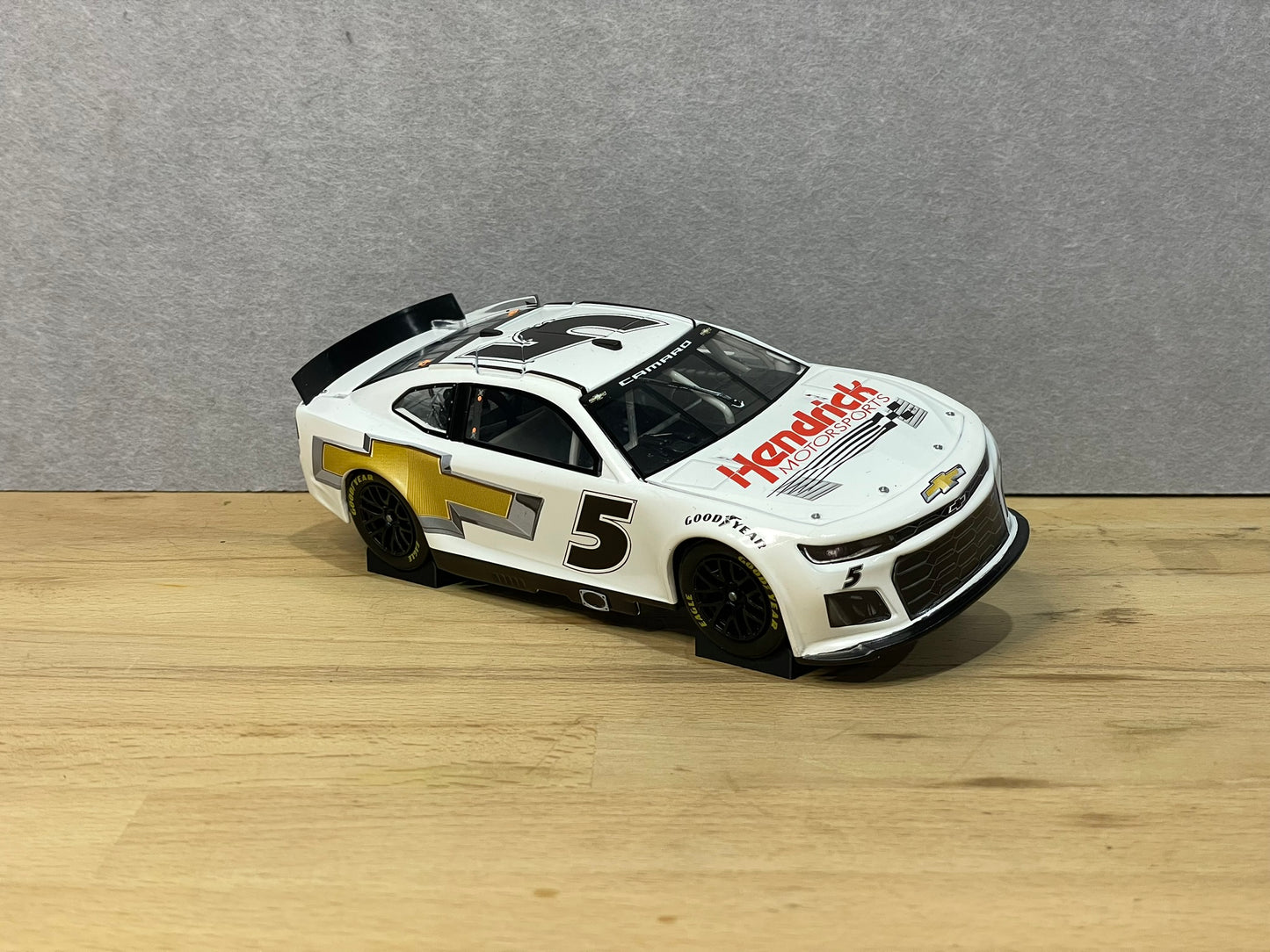 A 1:24 scale model of a NASCAR car displayed on two black angled display mounts on a wooden surface against a grey background.