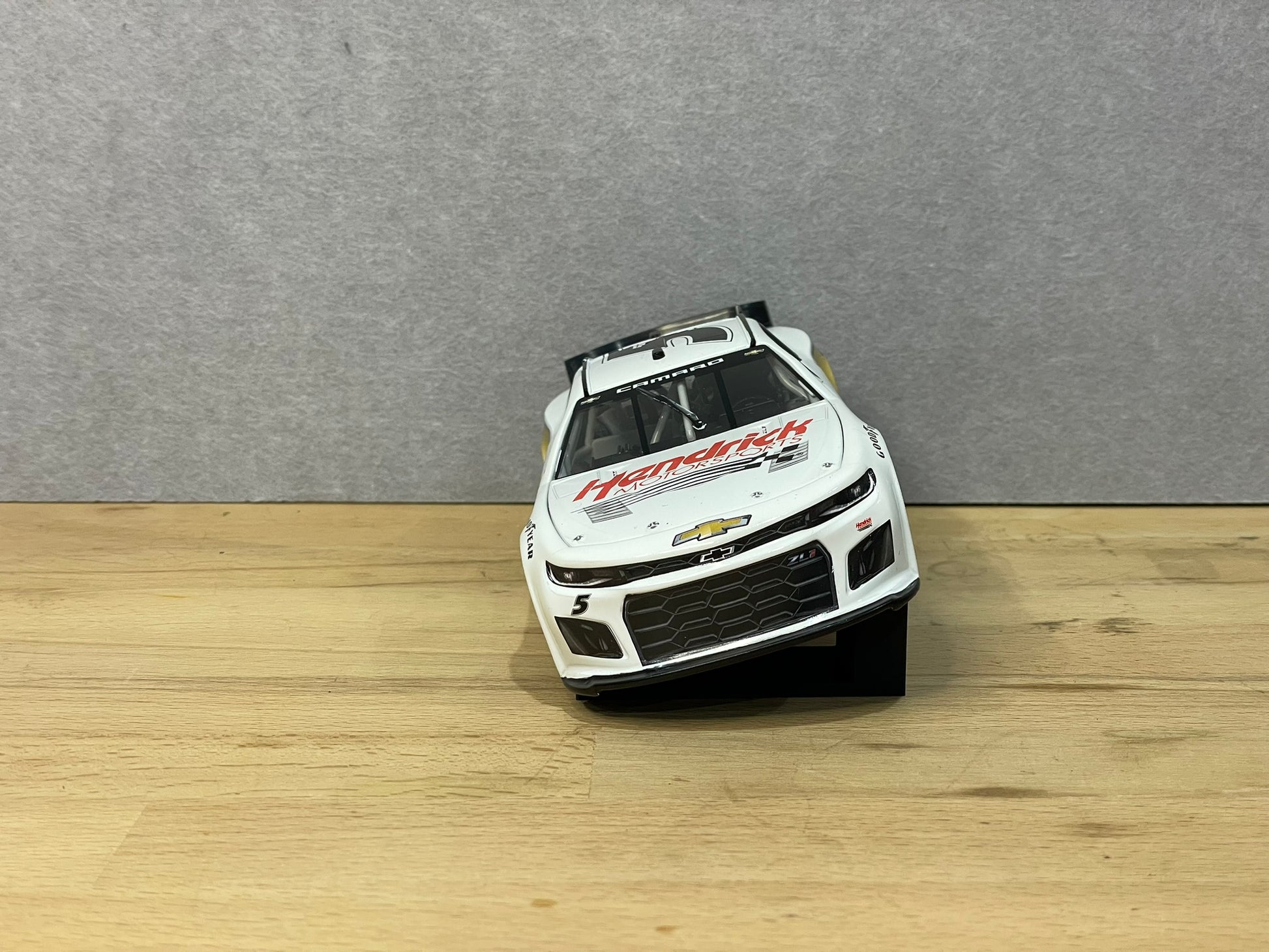 A 1:24 scale model of a NASCAR car displayed on two black angled display mounts on a wooden surface against a grey background.