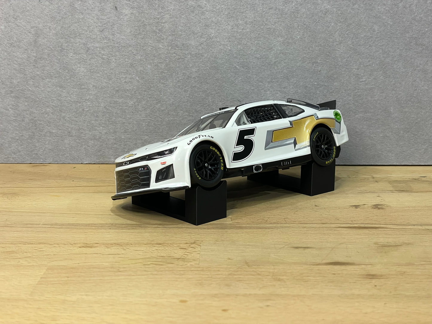 A 1:24 scale model of a NASCAR car displayed on two black angled display mounts on a wooden surface against a grey background.