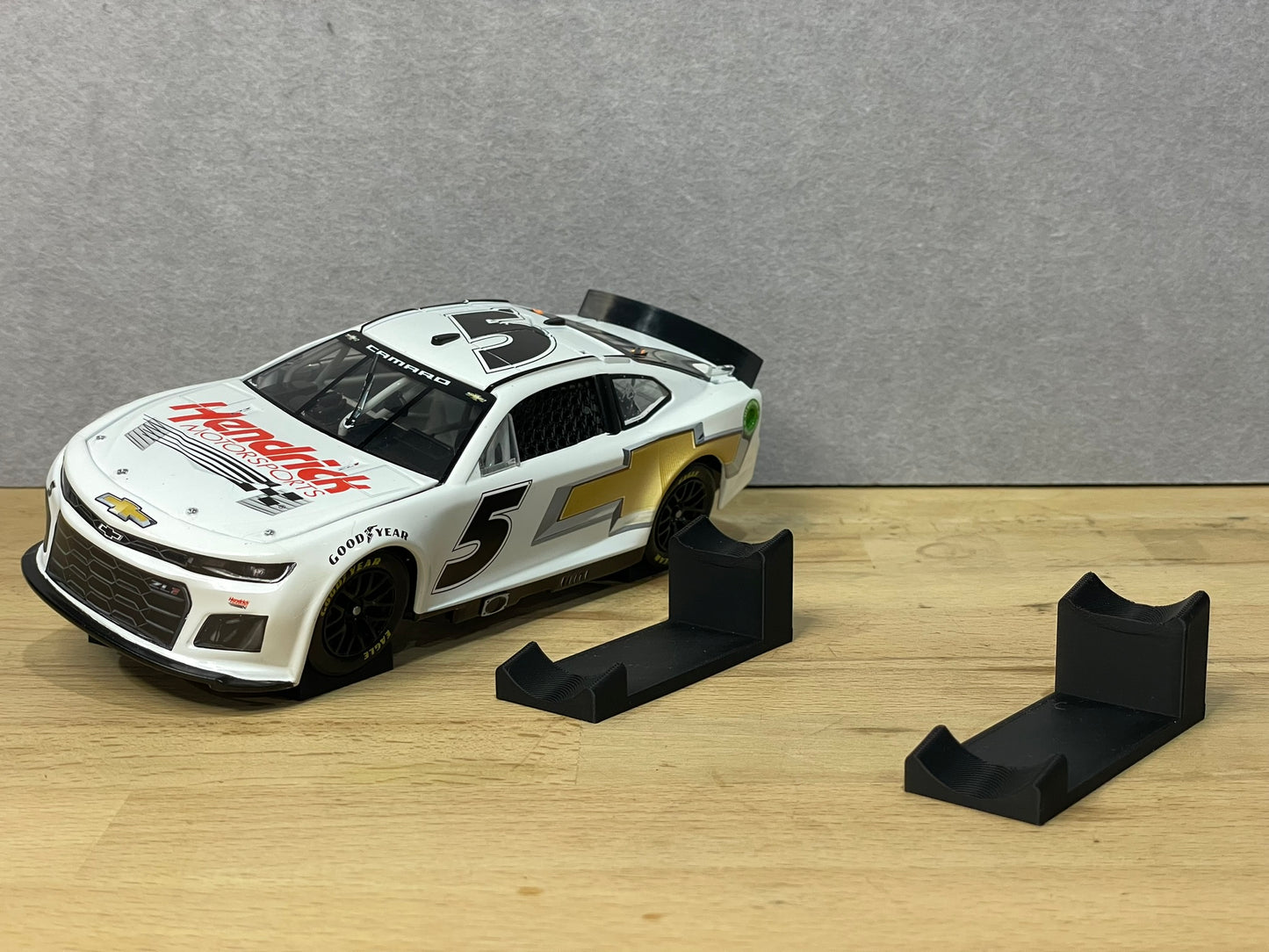 A 1:24 scale model of a NASCAR car displayed on two black angled display mounts on a wooden surface against a grey background.