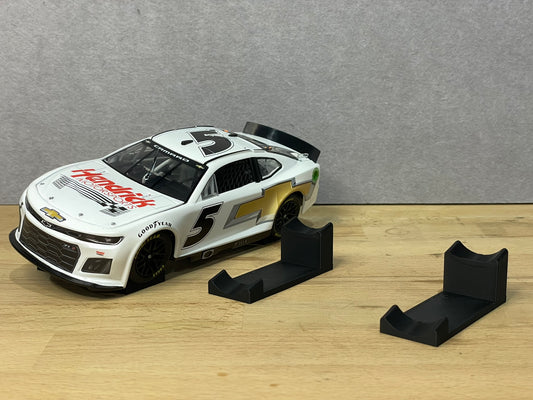A 1:24 scale model of a NASCAR car displayed on two black angled display mounts on a wooden surface against a grey background.